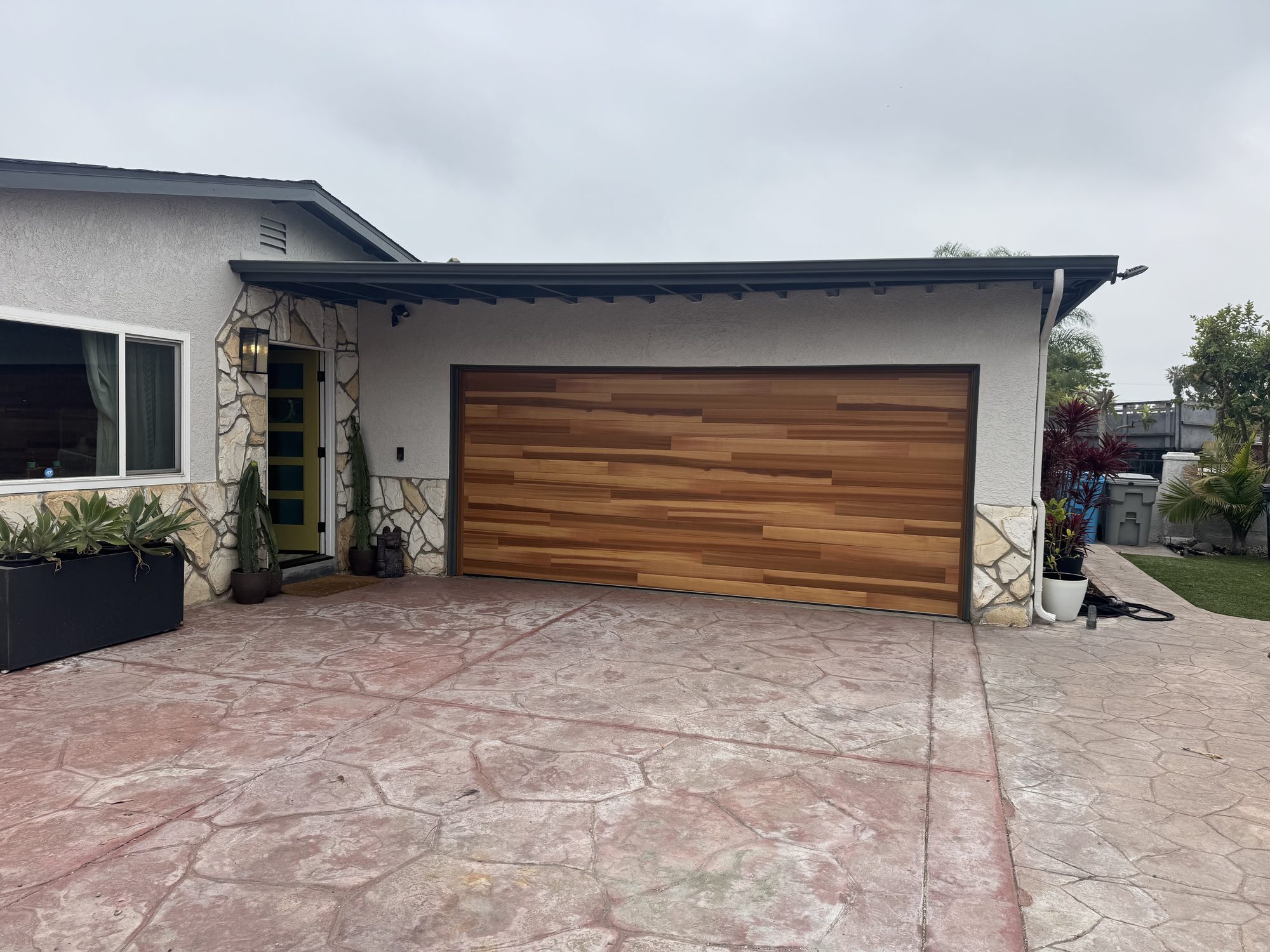 Clopay plank garage door in a warm natural wood tone with a dark bronze frame, installed on a mid-century ranch home in Poway, CA
