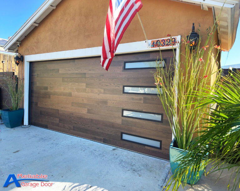 A stylish Clopay Plank garage door with frosted windows, flanked by vibrant green plants and an American flag, enhancing a San Diego home's exterior.